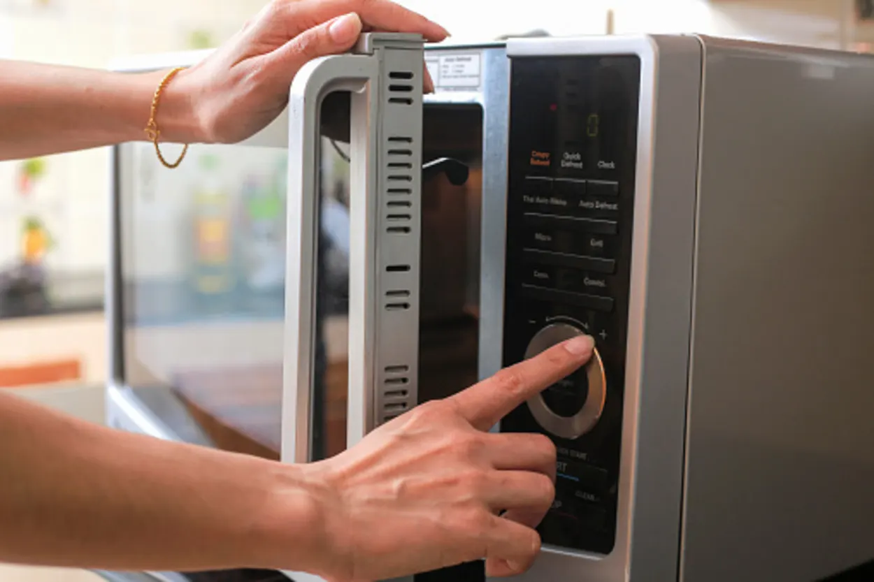 An image showing a woman setting microwave timer