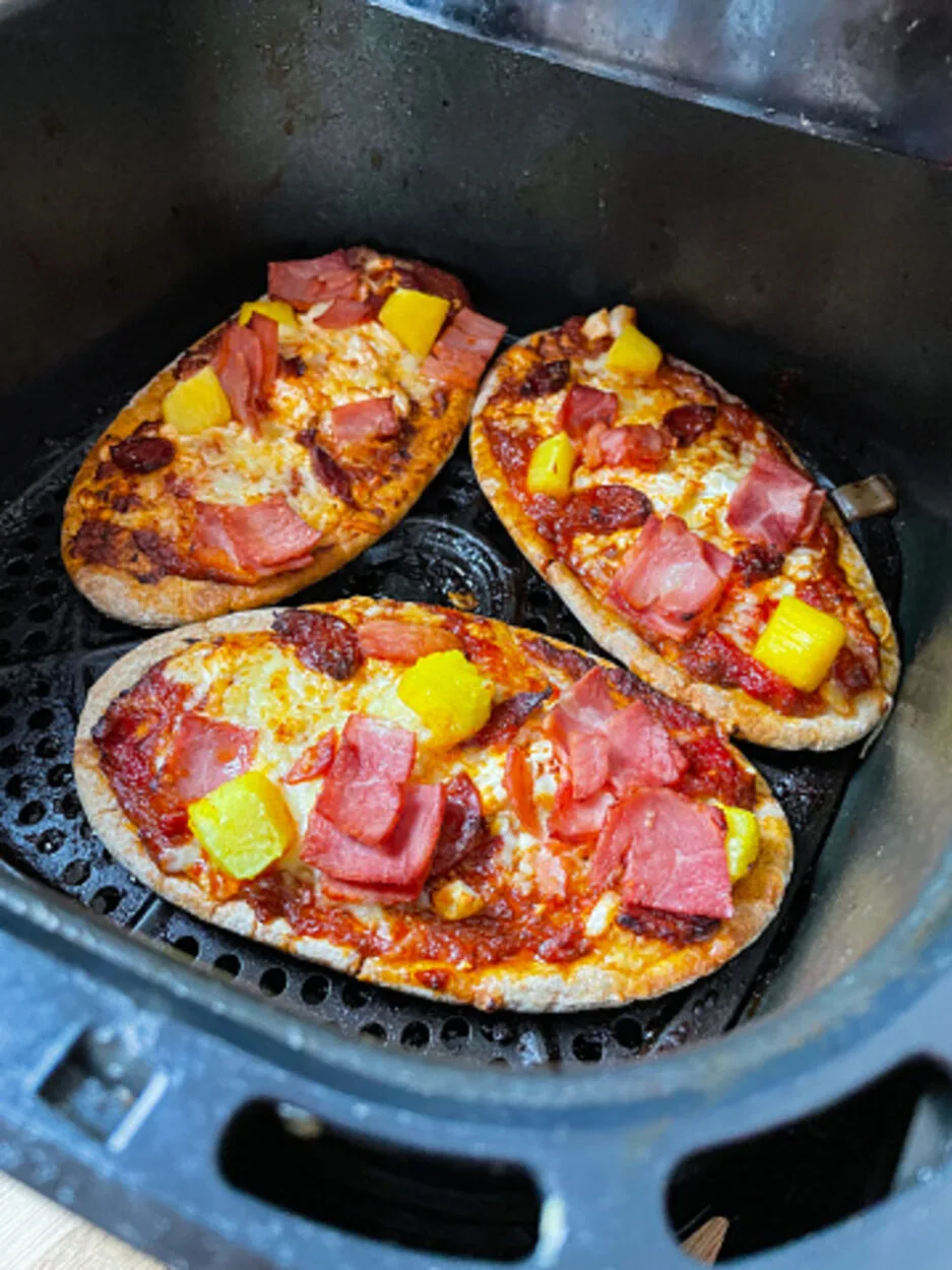 An image showing three pizzas in an air fryer topped with pepperoni and cheese