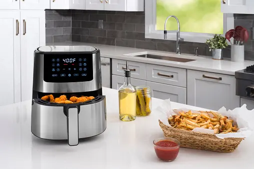 An air fryer with sauce and French fries placed beside it.