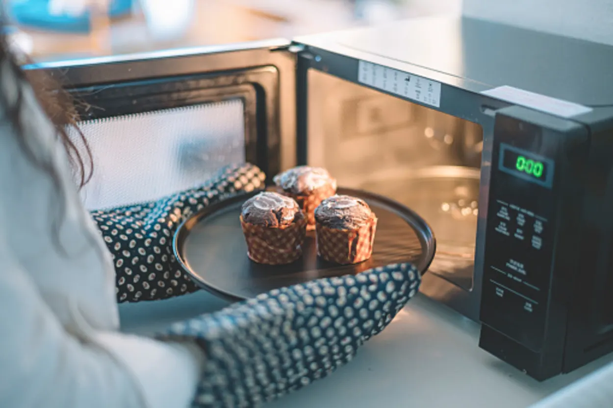 Lady with mittens on pulling out cupcakes from microwave