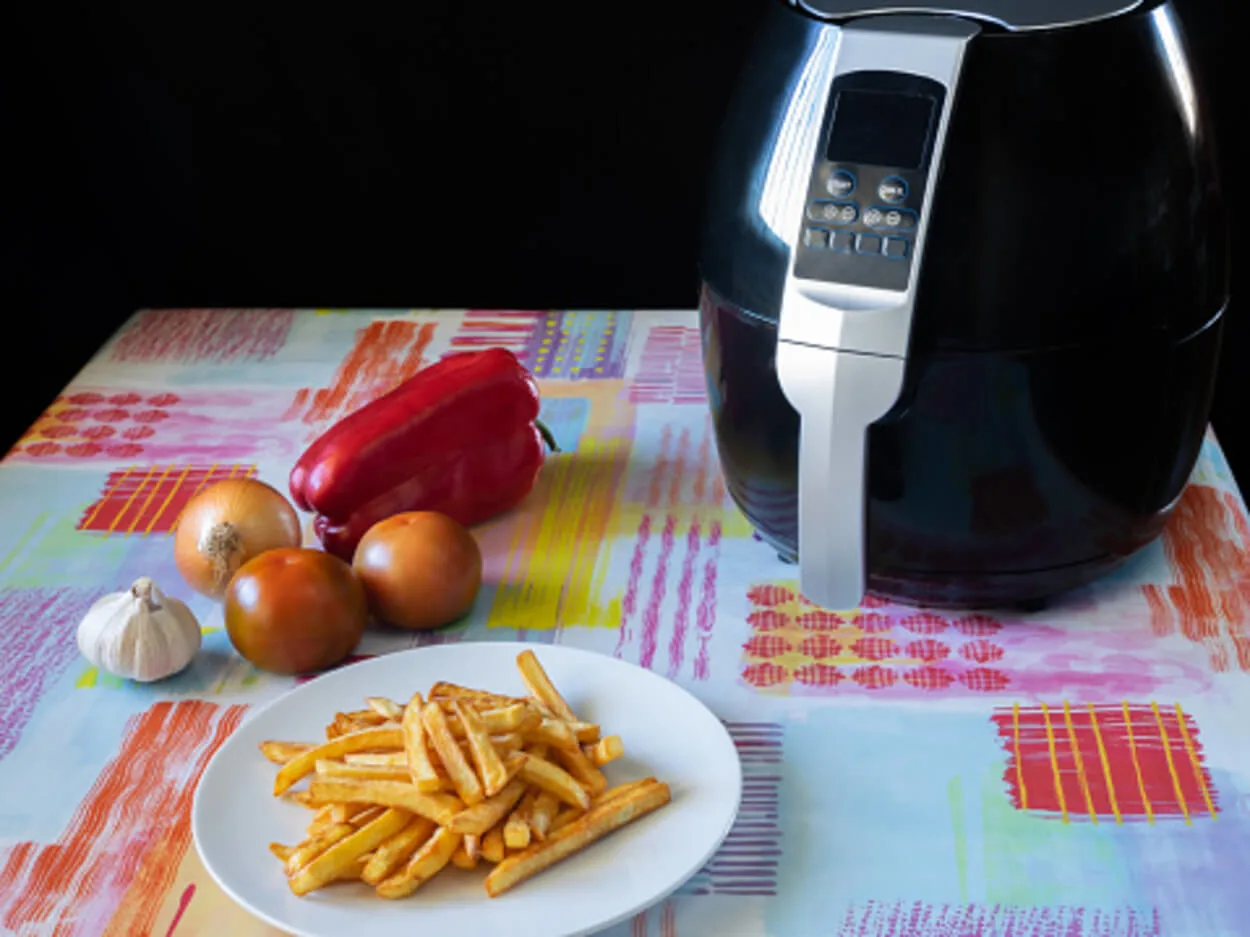 An air fryer placed on a table with French fries and some vegetables