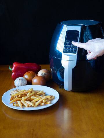 An air fryer and French fries cooked in it are placed aside