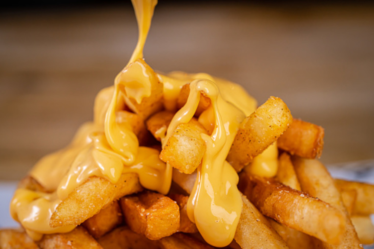 Cheese being poured on fried French fries.