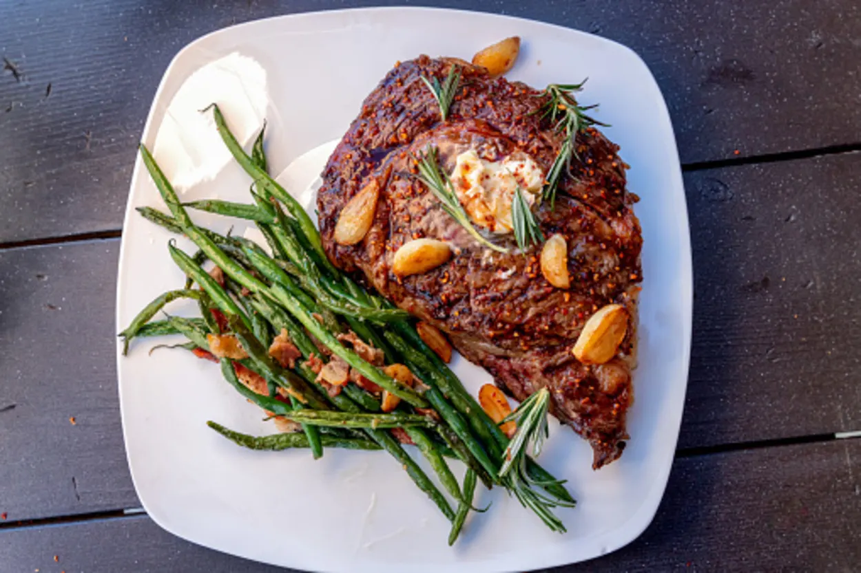 A platter of cooked rib eye with roasted garlic and beans
