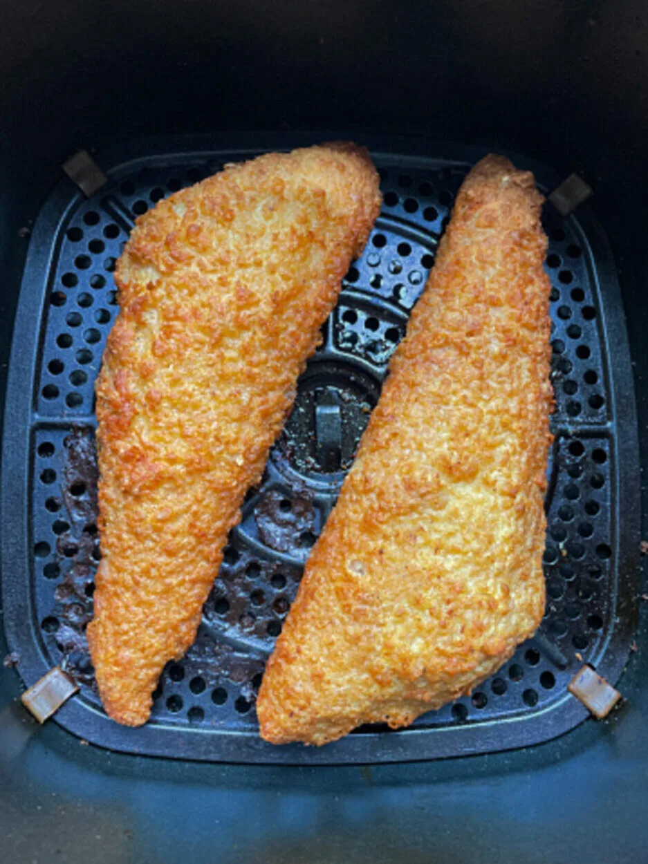 elevated view of the inside of an air fryer with golden brown, freshly cooked battered cod pieces. 
