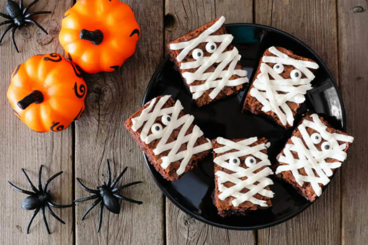 Brownie mummies on a round, black plate with a coupe of fake spiders and pumpkins 