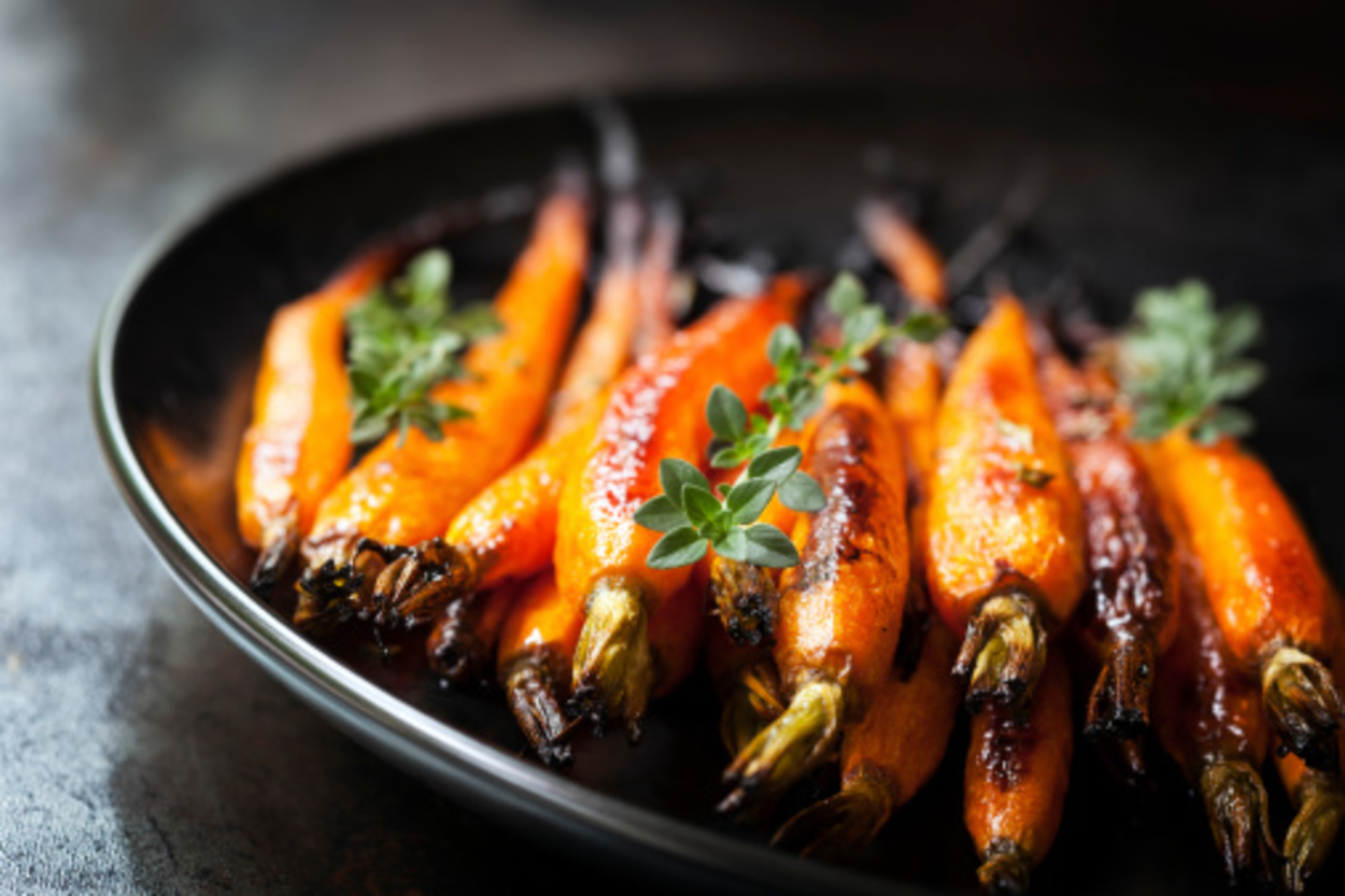 Oven-baked baby carrots with thyme, on a black plate over slate.