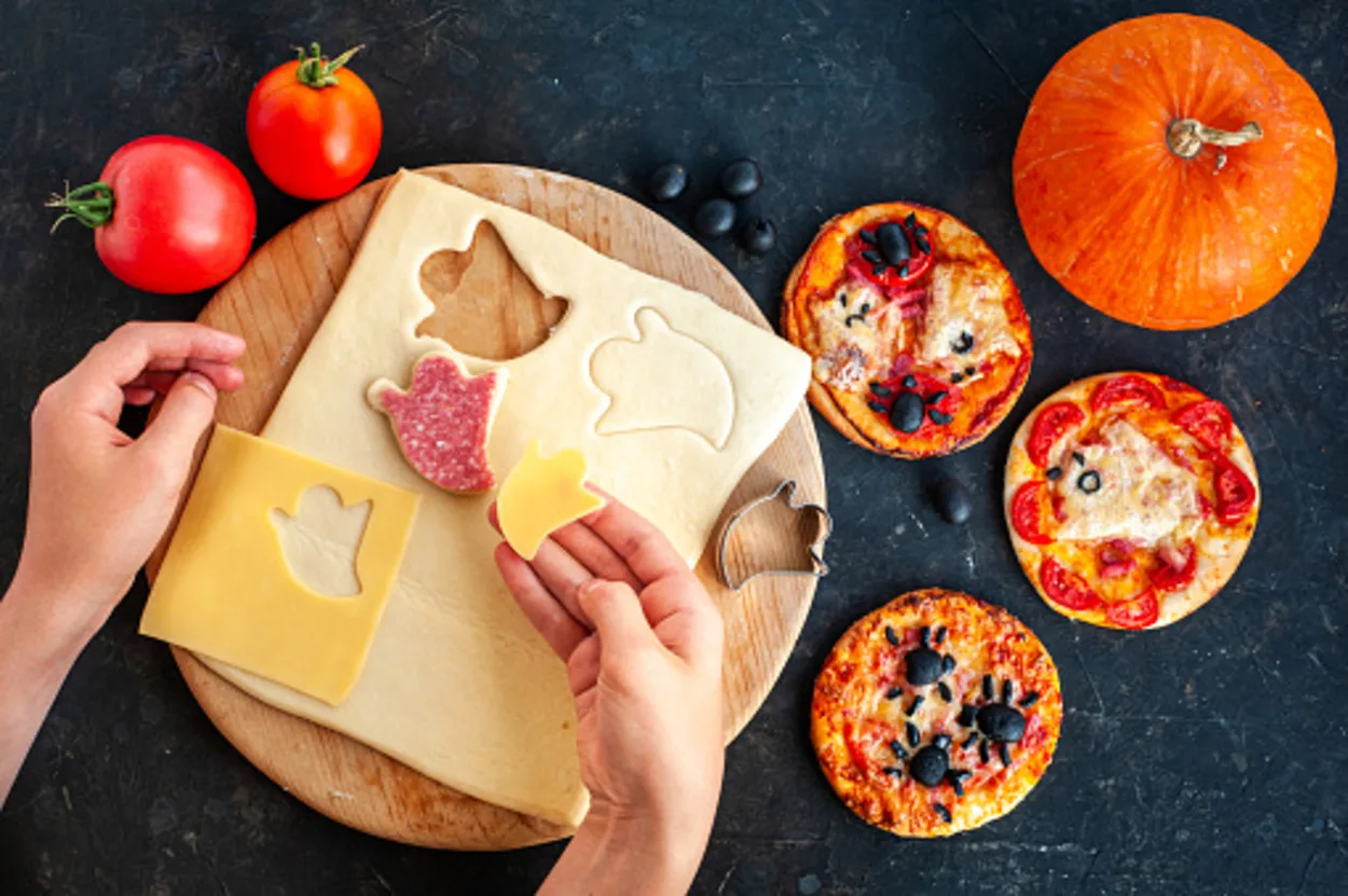 Woman making Halloween-themed toppings for mini pizzas.