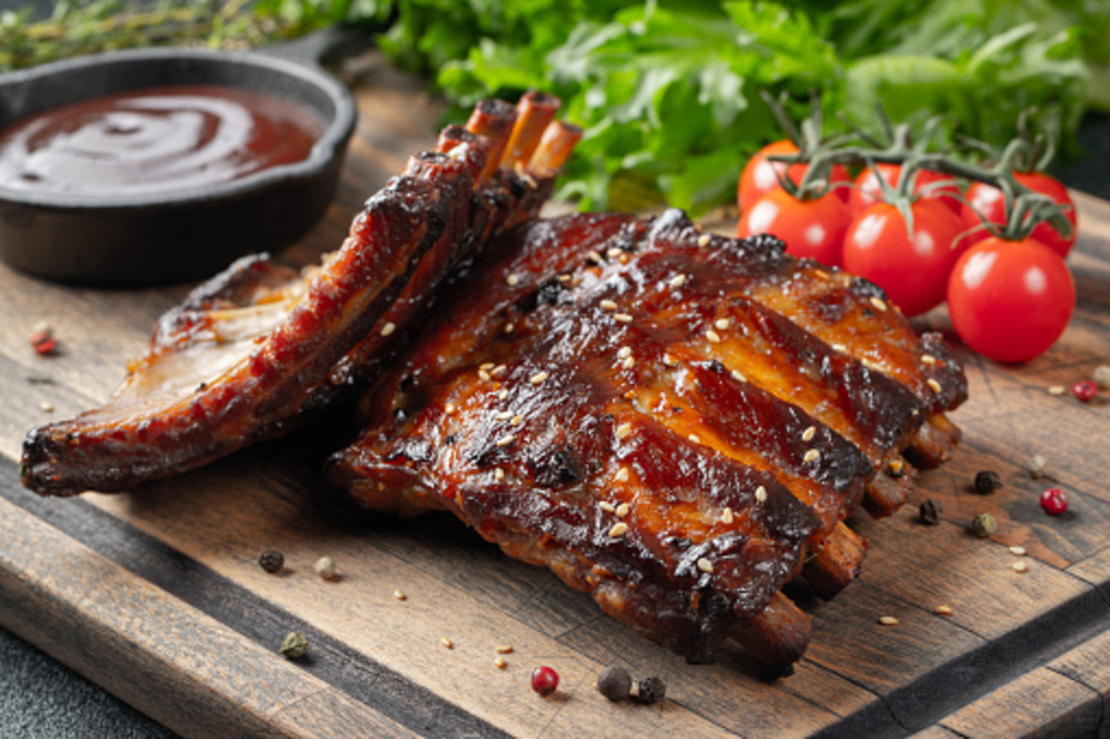 air fried BBQ ribs with cheery tomatoes and sacue on a wooden board