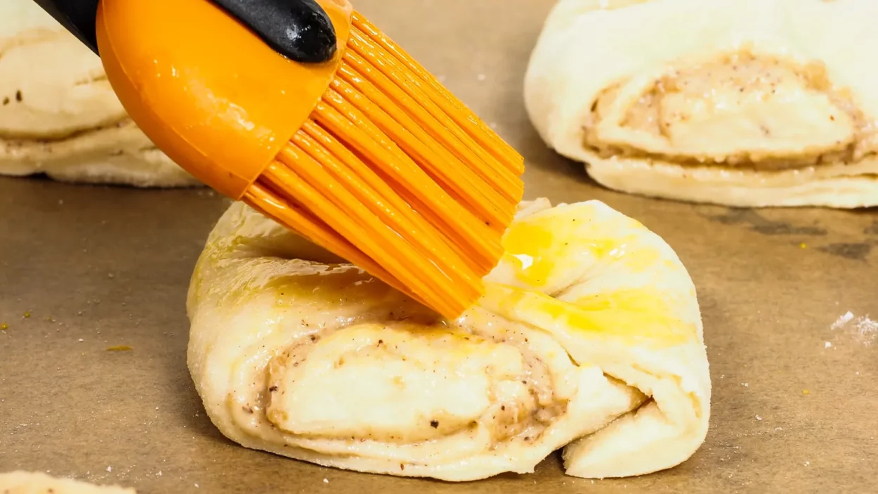 closeup of person glazing plaited baked goods with egg wash