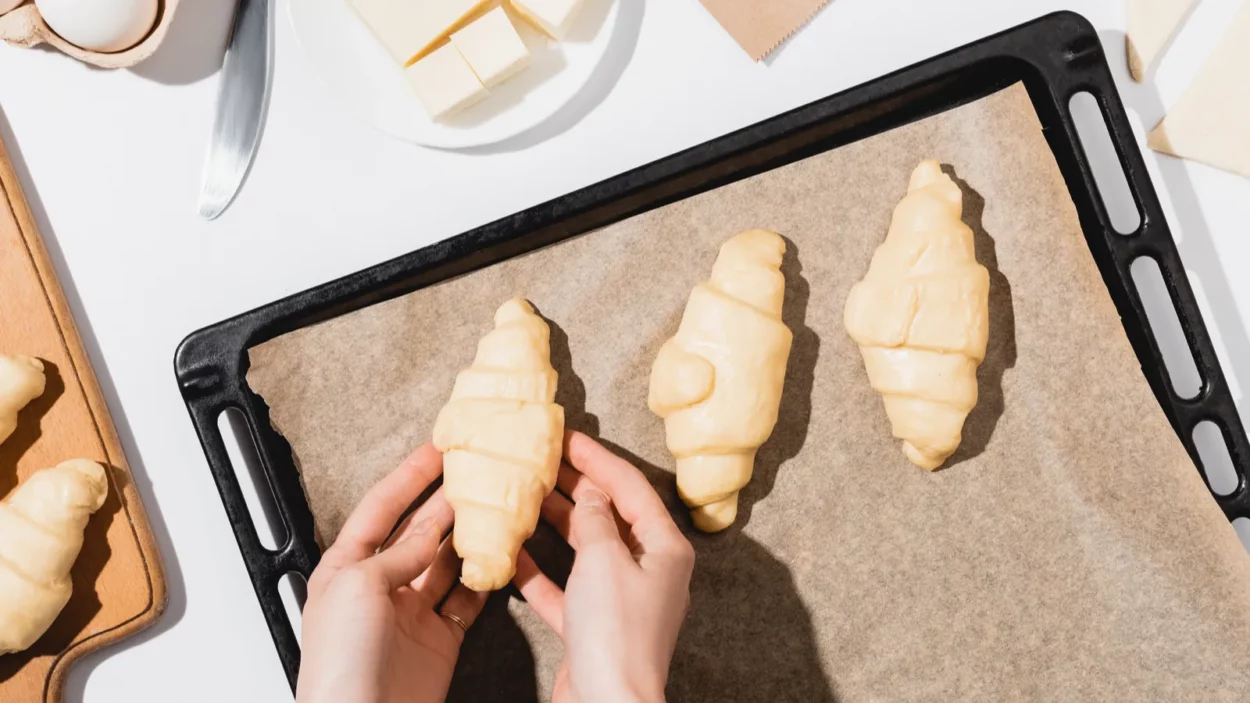 cropped view of woman putting croissants on baking tray on