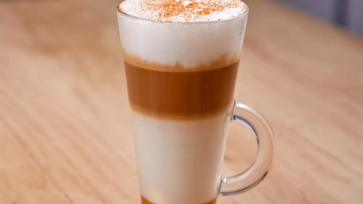 Latte macchiato with syrup in glass on wooden background close up.