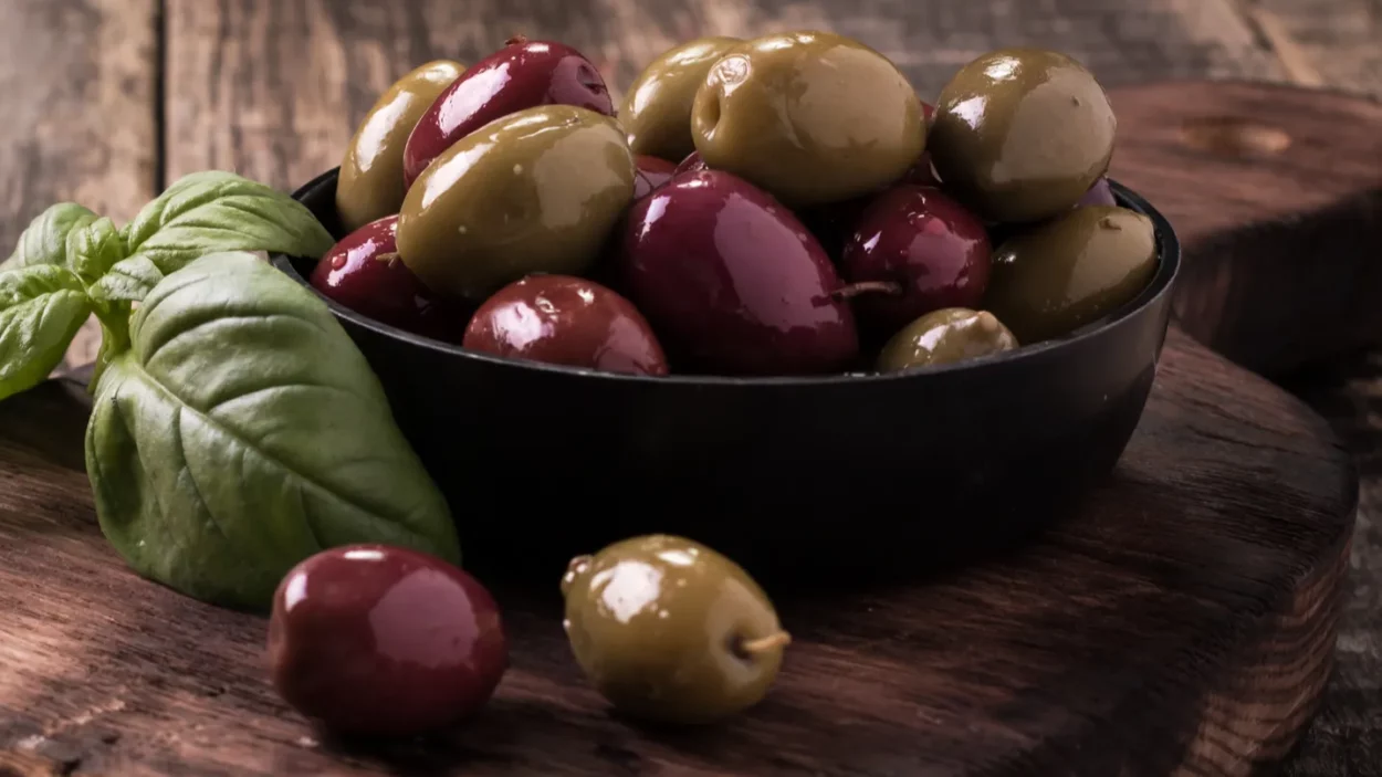 Olives on wooden dark table with basil.