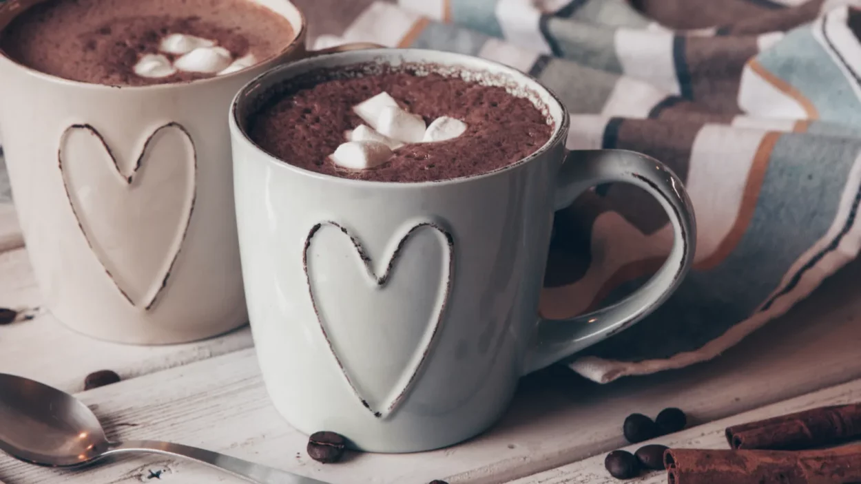 two cups of hot cocoa with marshmallows and cinnamon sticks