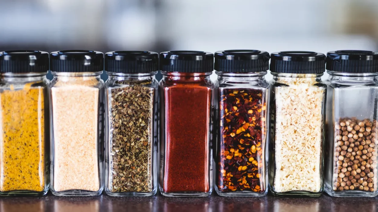 Spices seeds and seasonings in matching spice jars on tidy pantry shelf.