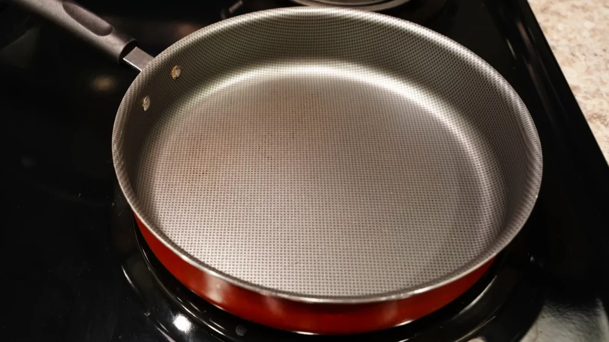 An empty red and grey frying pan Skillet sits on the stove top.