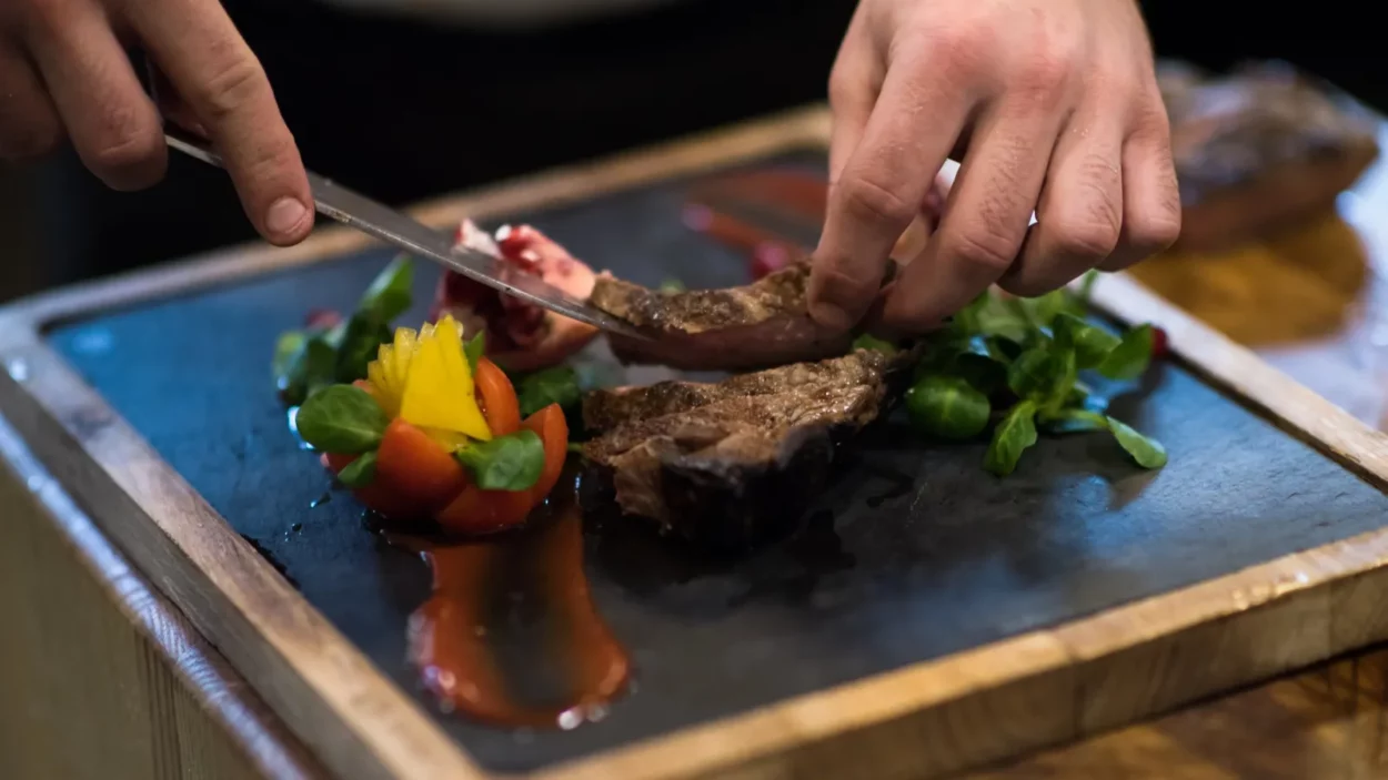 Closeup of Chef hands in hotel or restaurant kitchen serving beef steak with vegetable decoration.