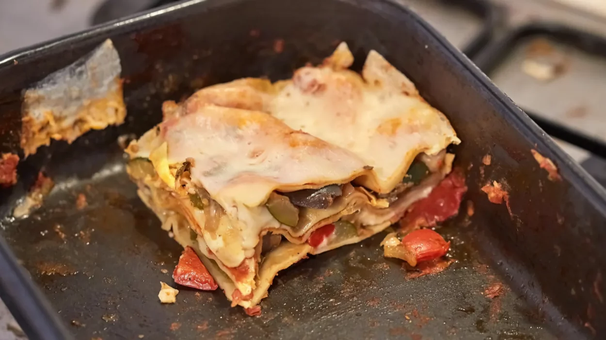 Lasagne leftover food in a pan on a dirty kitchen stove.