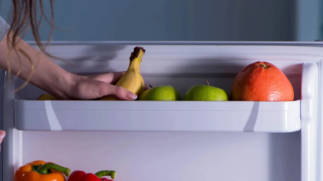 Woman putting fruits in freezer door shelf.