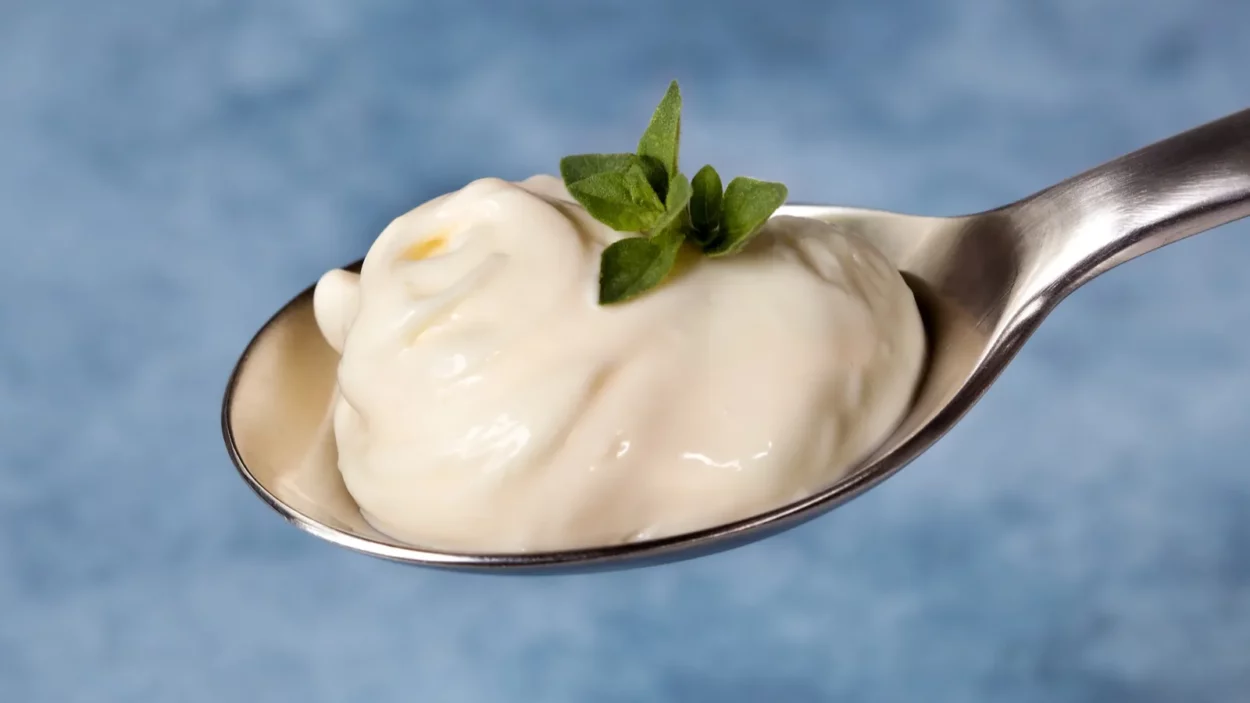 A spoonful of mayonnaise with herbs, over blurred blue background.