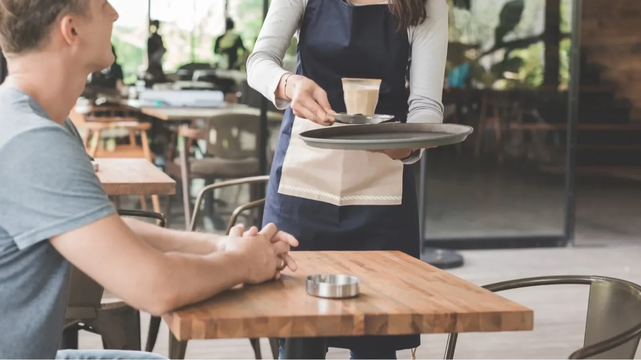 Portrait of a female waitress serving coffee to a male customer.