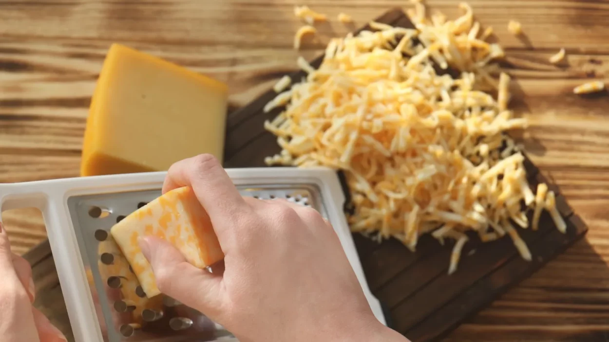 Woman grating cheese on wooden table.