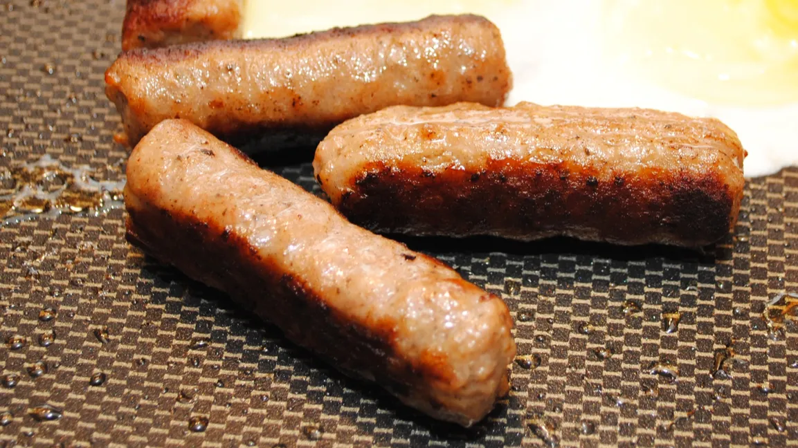 Cooking three sausages in pan.