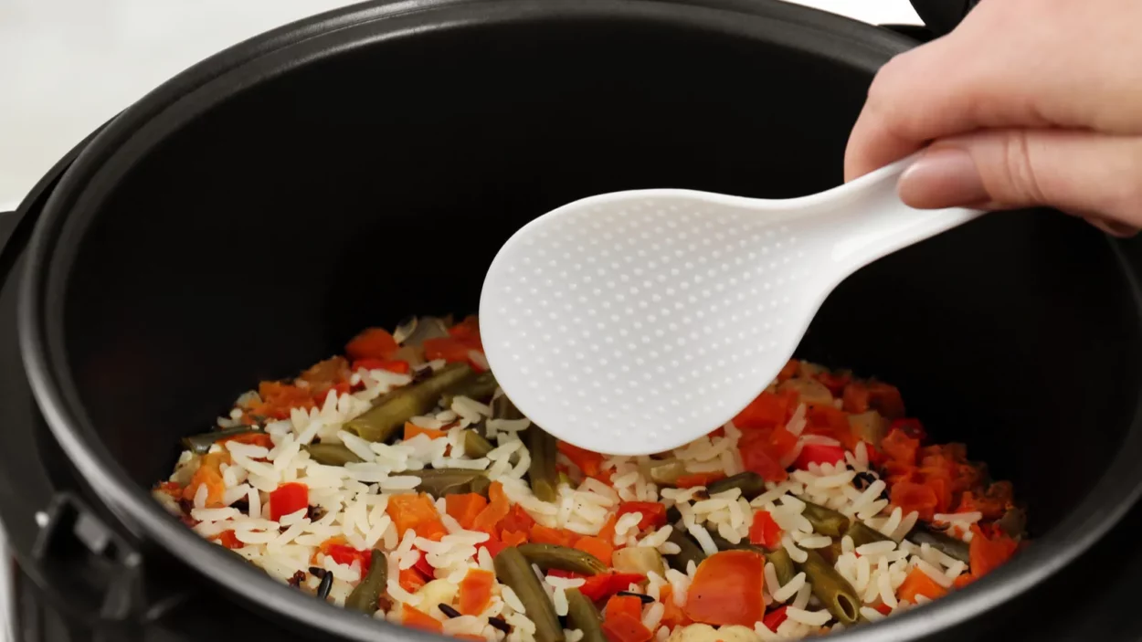 Woman preparing rice with vegetables in multi cooker, closeup.