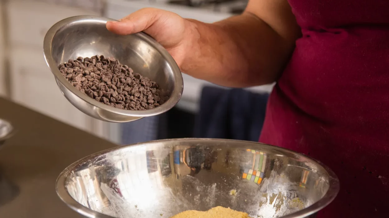 Young woman's hands putting chocolate chips into cookie mix.