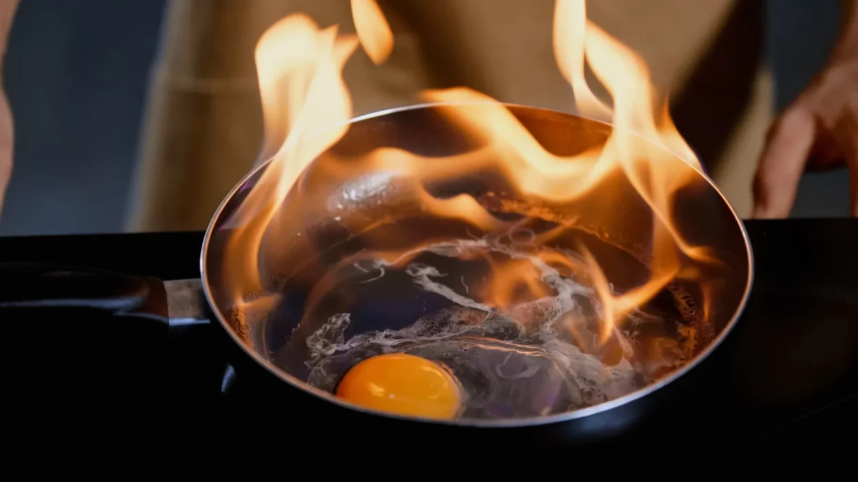 cropped view of man frying chicken egg with fire on