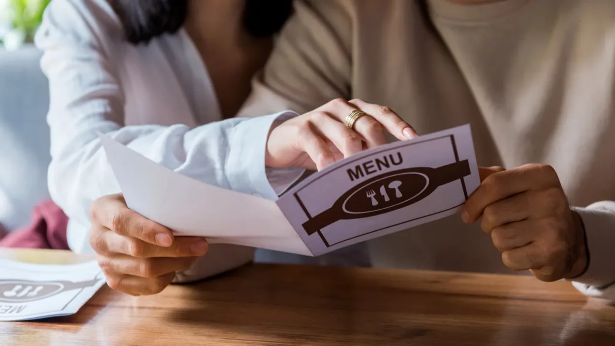 Cropped view of woman pointing with finger at menu near happy man.