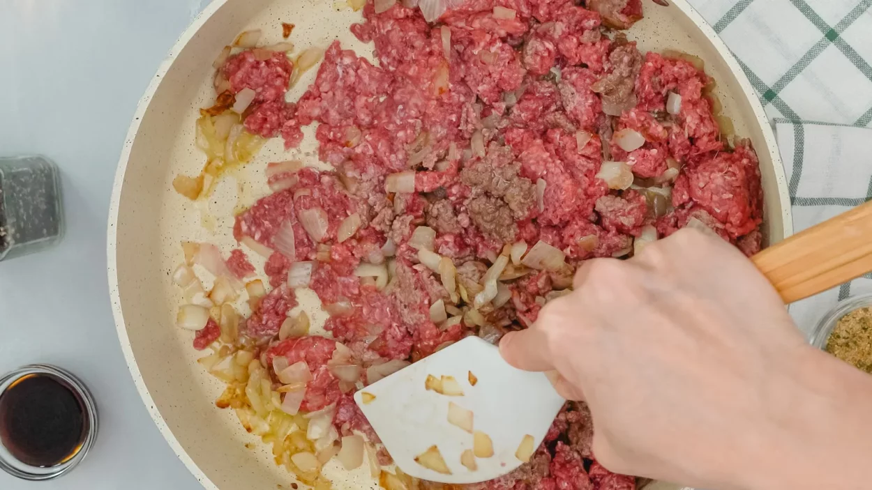 ground beef and chopped onion chef mixing raw ingredients on