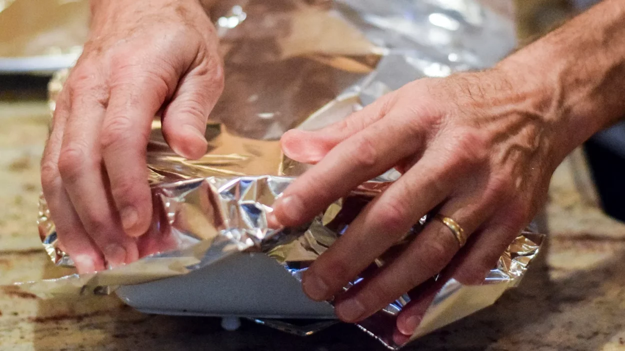 Hands covering casserole dish with aluminum foil to back in oven.