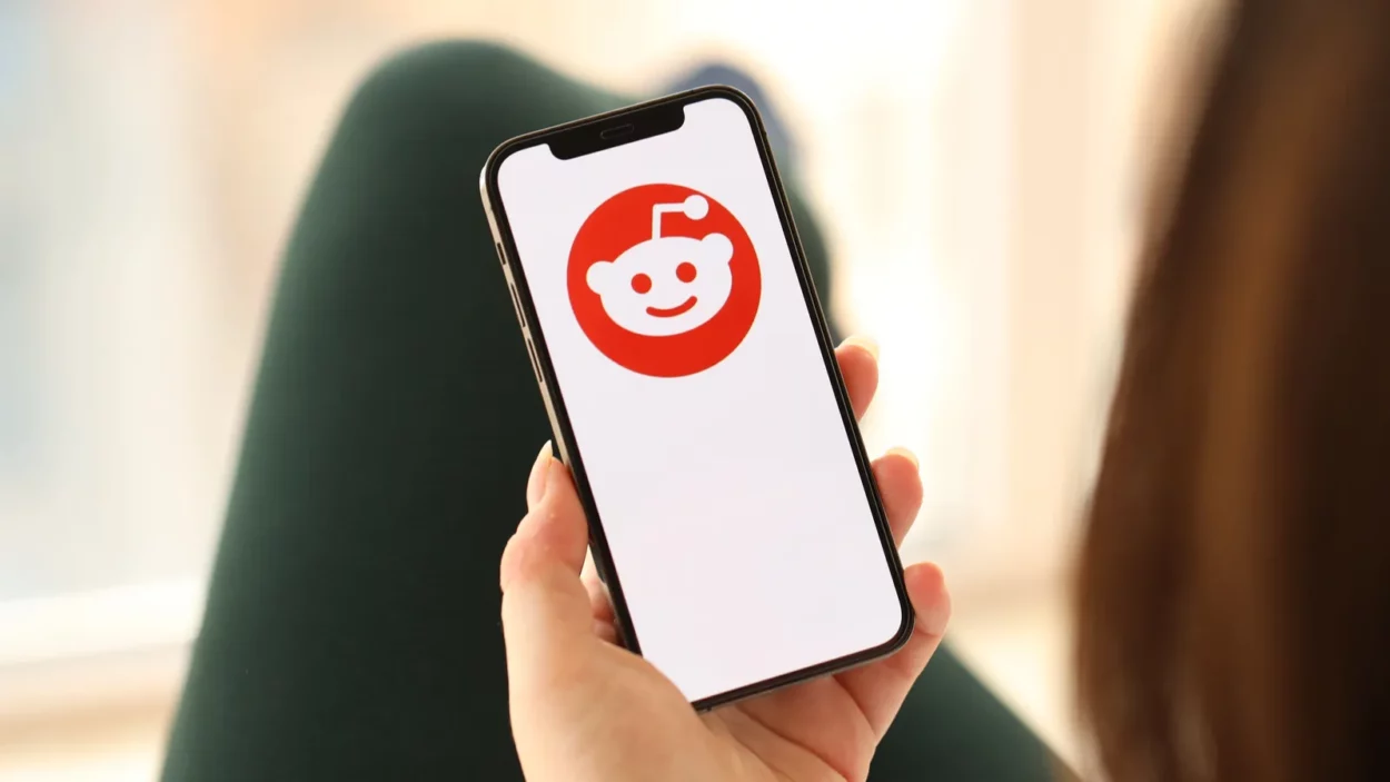 Reddit icon on smartphone screen in young female hands indoors.