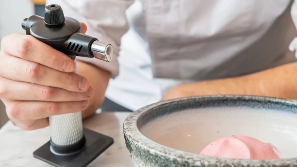 Professional chef holding a kitchen torch to be used in one of his creations.