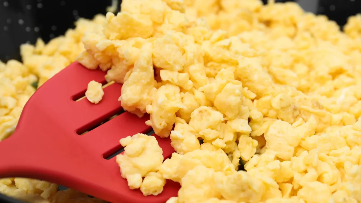 Stirring tasty scrambled eggs in wok pan closeup.
