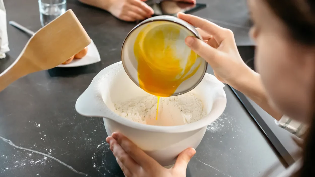 Unrecognizable young girl adding eggs to flour while baking a cake.