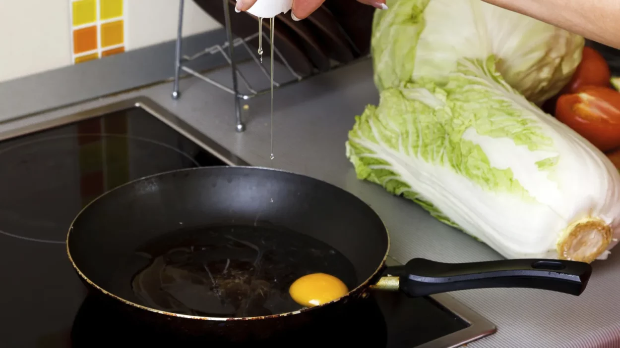 woman cracking eggs into frying pan in kitchen