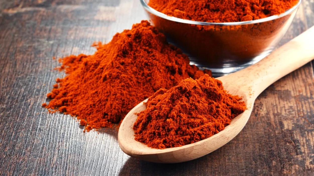 Composition with bowl of chili powder on wooden table.