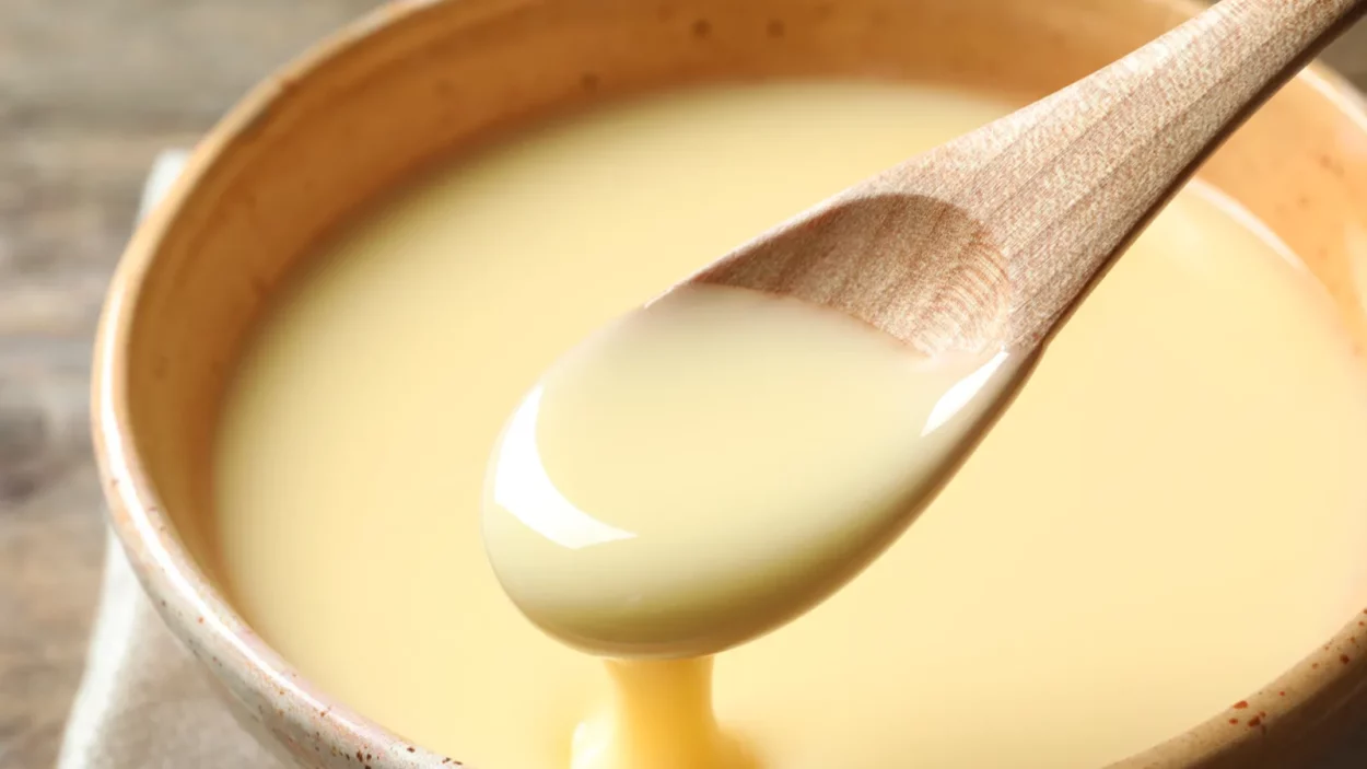 spoon of pouring condensed milk over bowl on table closeup