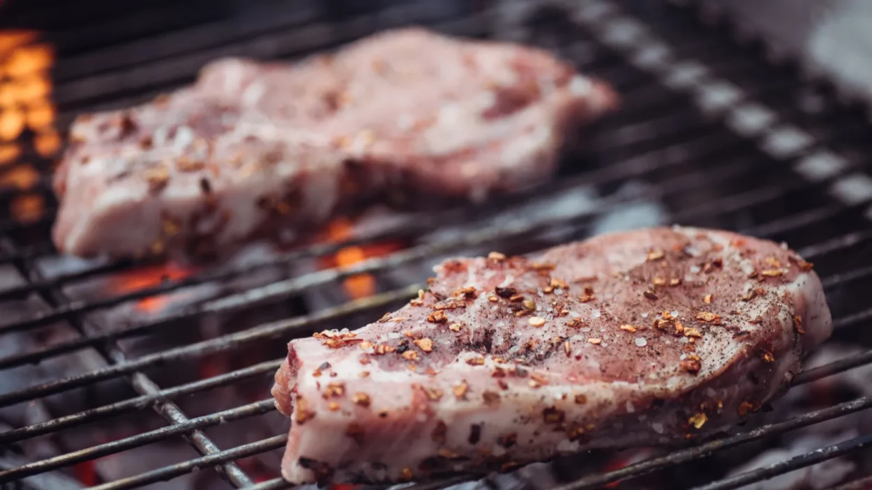 Selective focus of juicy raw steaks grilling on barbecue grid.